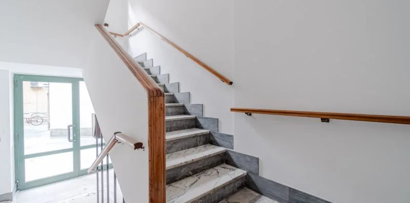 An indoor staircase with gray steps and wooden handrails beside a glass door.