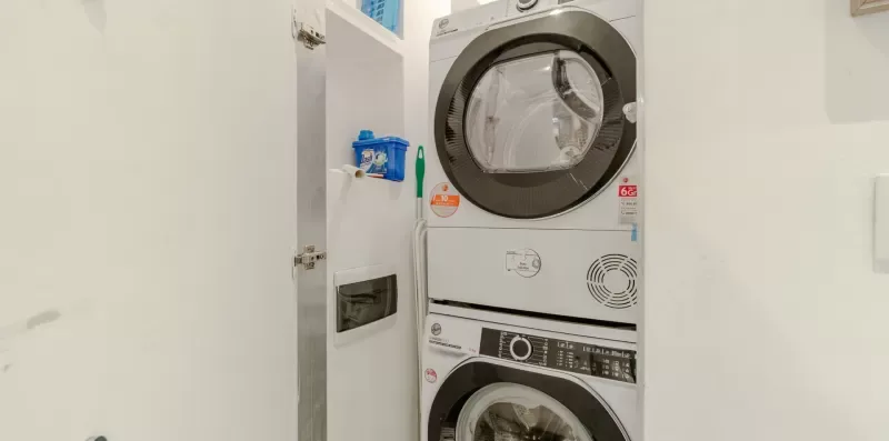 A laundry area with a stacked washer and dryer beside an open cabinet.