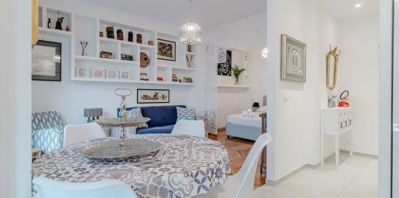 A bright living and dining area with patterned seating and wall shelves.