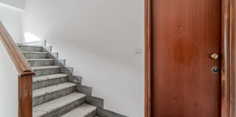 An indoor stairway with gray steps beside a wooden entry door.