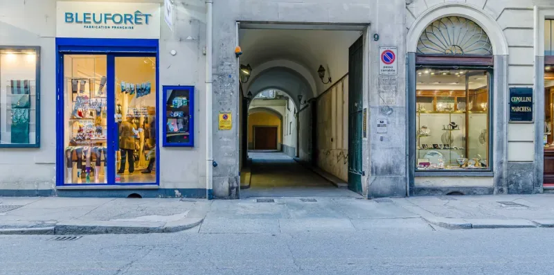 A city street storefront stands beside an arched passageway through a building.