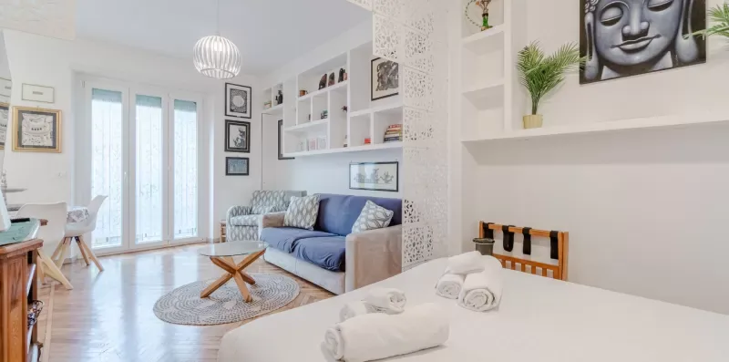 A bright living room with a blue sofa and a white dining area.