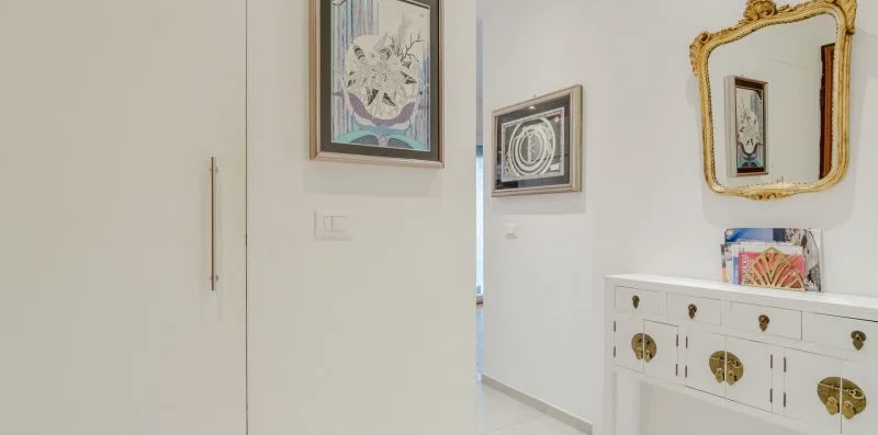 A bright hallway with framed artwork and a white console beneath a mirror.