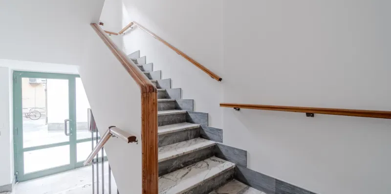 An indoor staircase with gray steps and wooden handrails.
