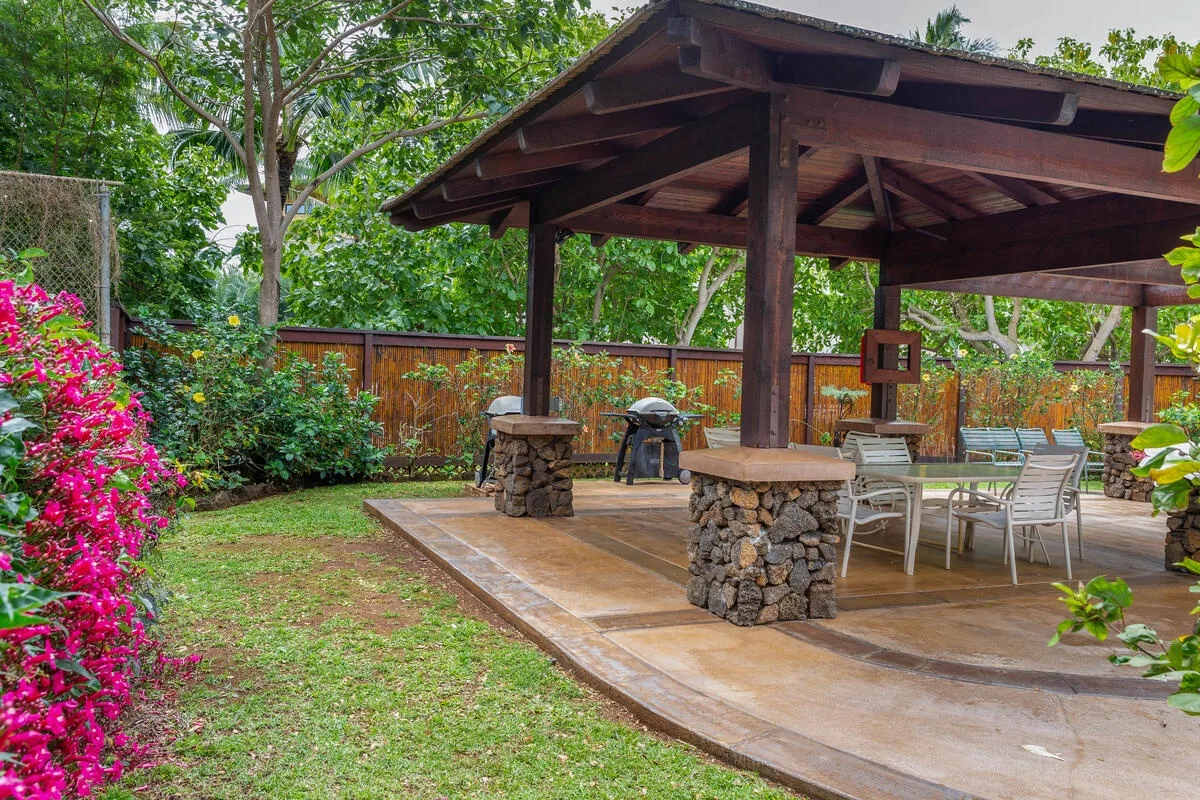 Un patio exterior cubierto con asientos y una mesa de comedor junto a un jardín.