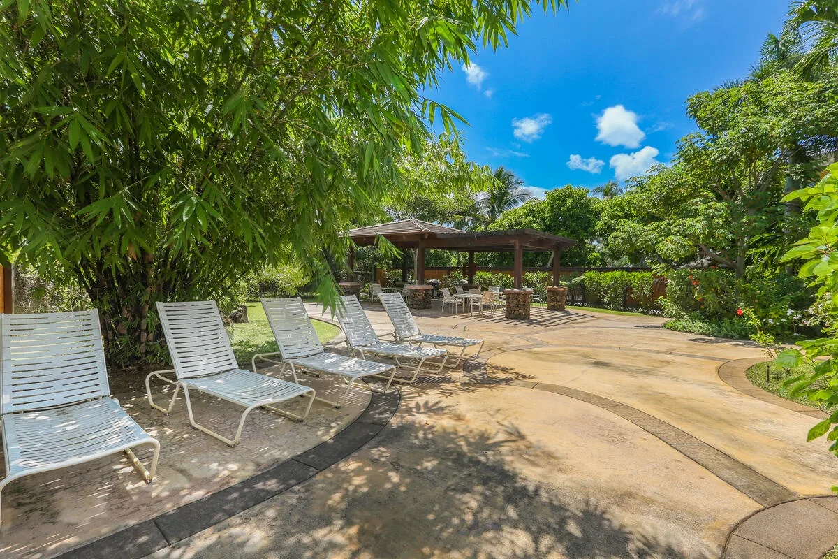 Un patio al aire libre con asientos de descanso, árboles y una pérgola sombreada.