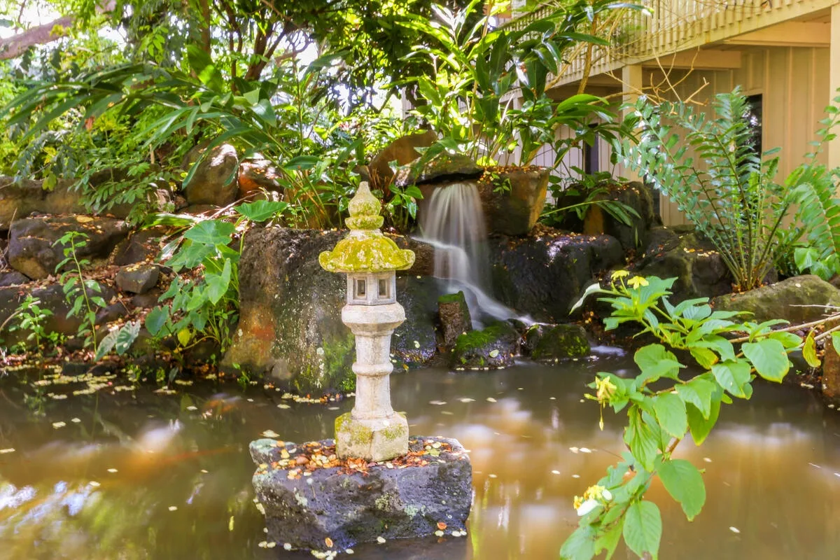 Un estanque de jardín con una pequeña cascada y una linterna de piedra.