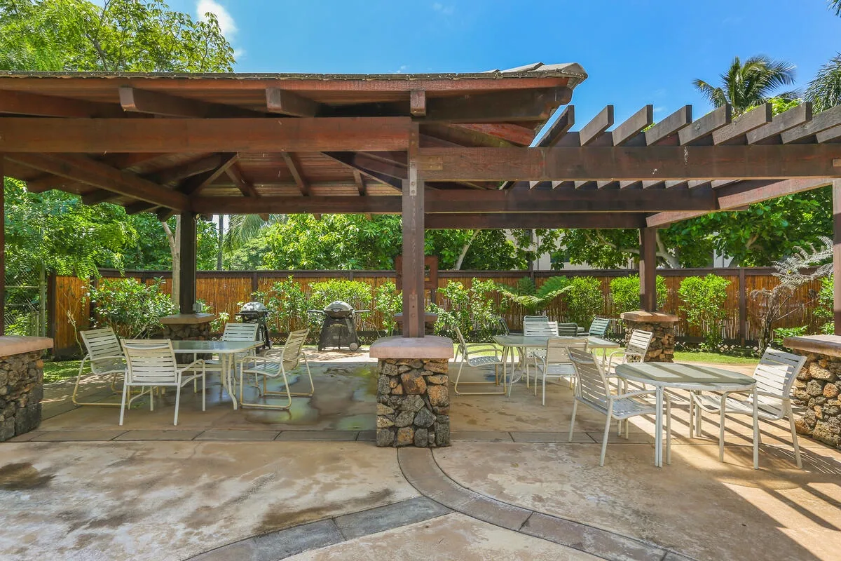 Un patio al aire libre con mesas y asientos bajo una pérgola de madera.