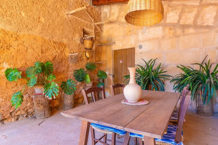 A rustic dining area with a wooden table, chairs, and potted plants.