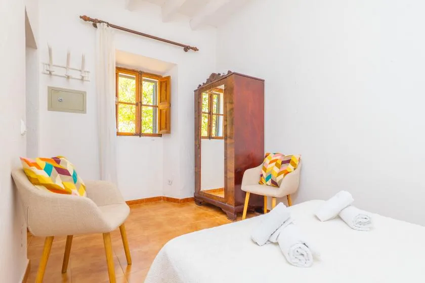 A bright bedroom with a bed, two chairs, and a window.