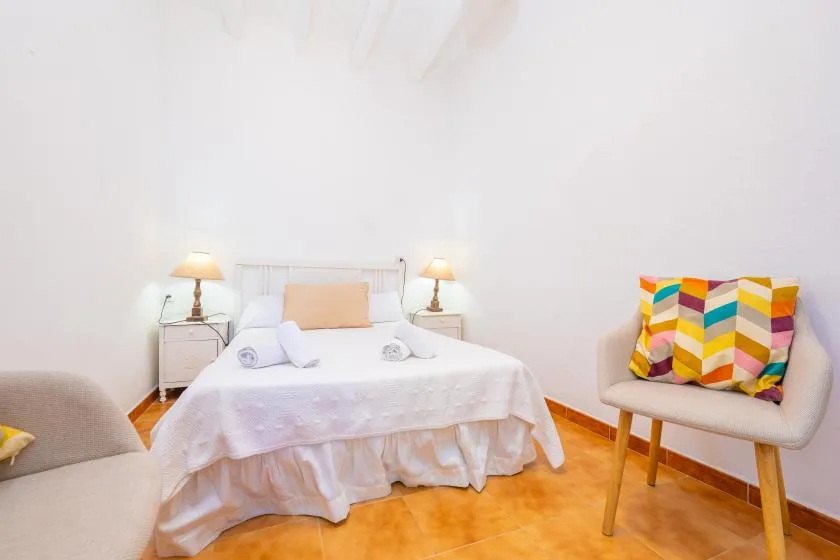 A bright bedroom with a neatly made bed and colorful seating.