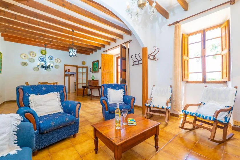 A bright living room with blue seating, a wooden coffee table, and exposed ceiling beams.