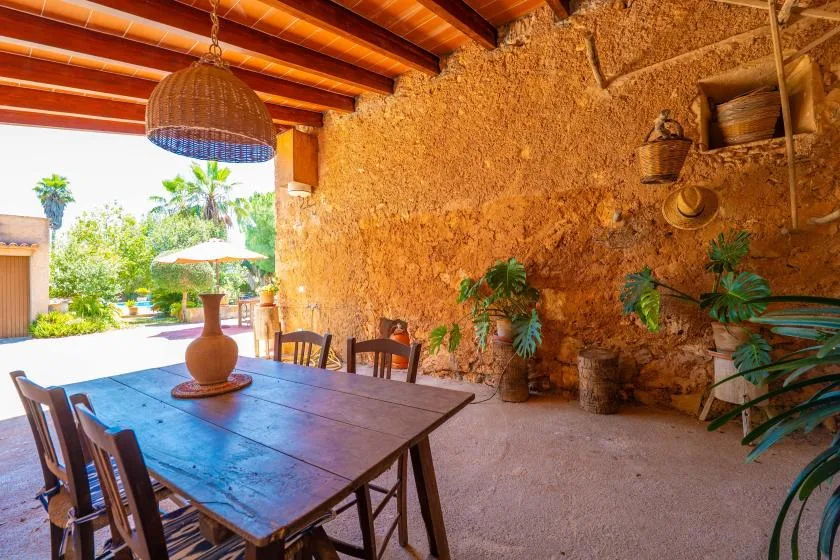 A rustic dining area with a wooden table, chairs, and potted plants.