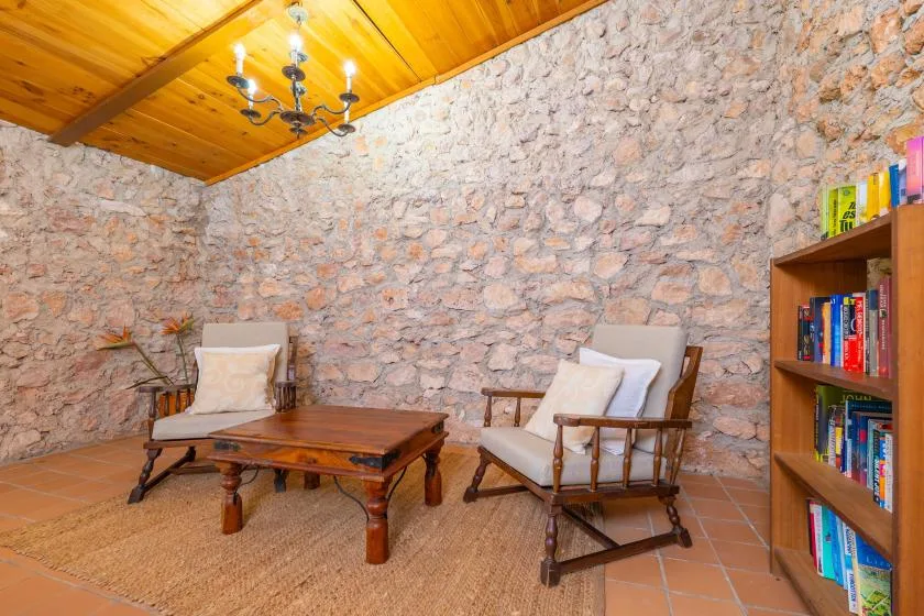 A rustic sitting area has cushioned seating, a wooden coffee table, and a bookshelf.