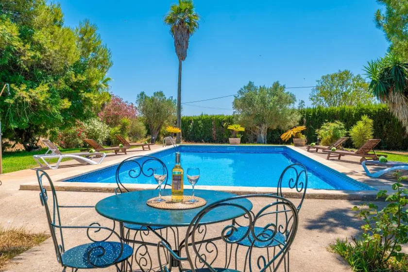 An outdoor swimming pool is surrounded by lounge chairs, with a patio table in the foreground.