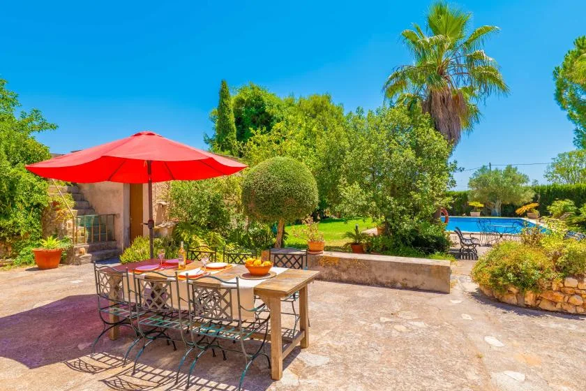 Outdoor patio with a dining table and red umbrella, overlooking a garden and swimming pool.
