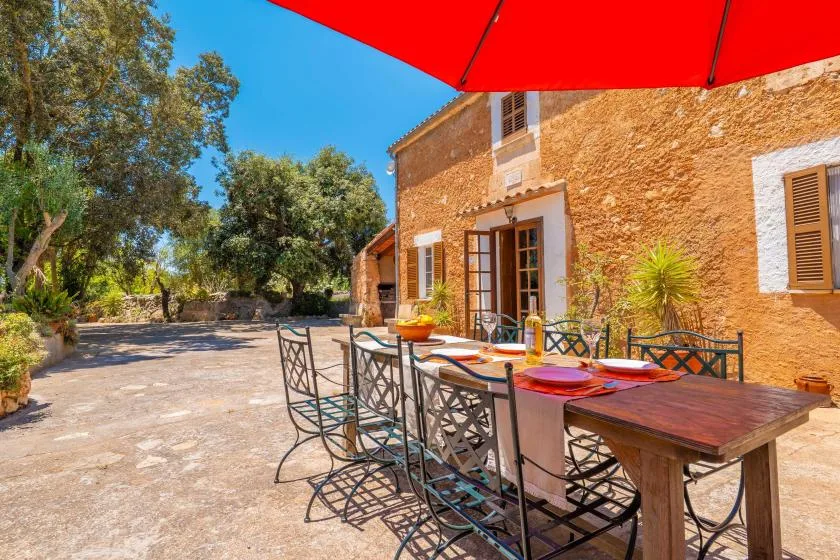 An outdoor dining table sits beside a stone house on a sunny terrace.
