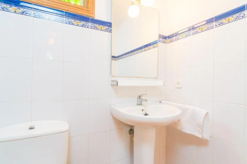 A tiled bathroom with a sink, mirror, and part of a toilet.