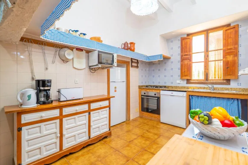 A bright kitchen with white cabinets, a refrigerator, and a wooden-framed window.