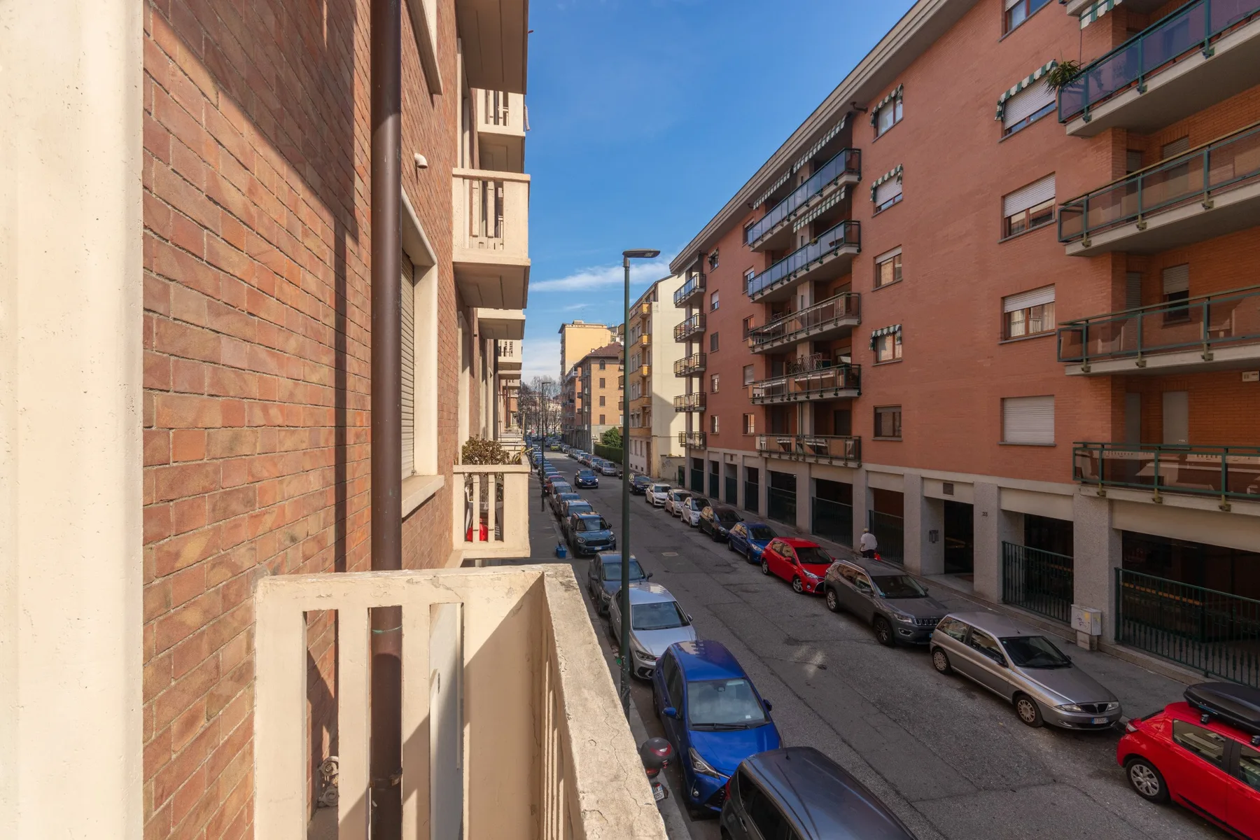 Una calle urbana estrecha bordeada de edificios de apartamentos y coches aparcados.