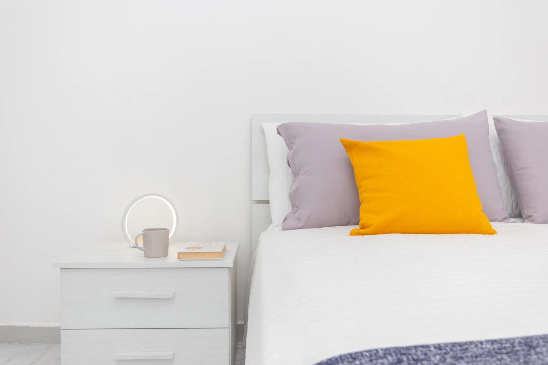 Un dormitorio con ropa de cama blanca y un cojín amarillo brillante.