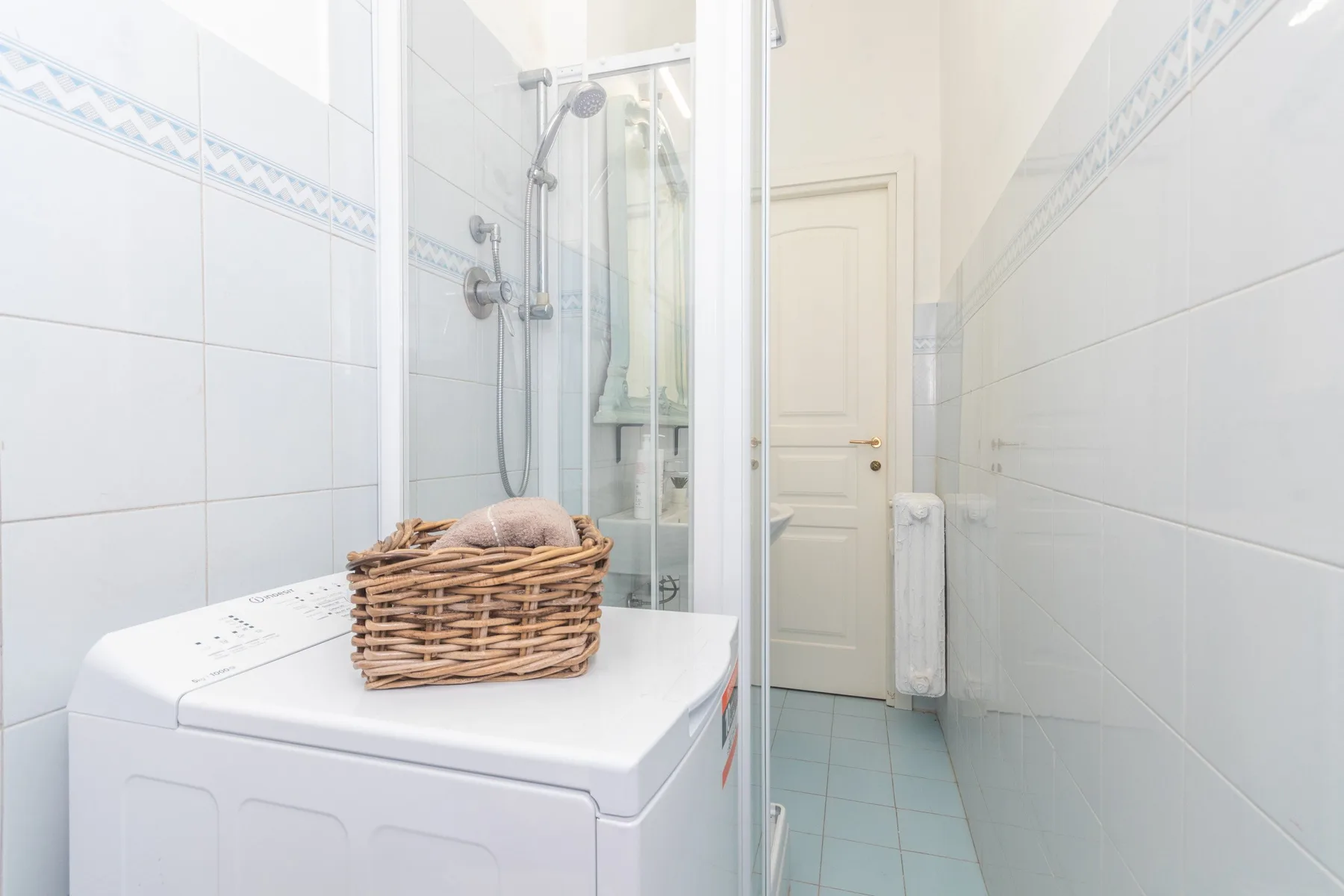 Un baño alicatado con ducha de vidrio, lavadora y puerta cerrada.