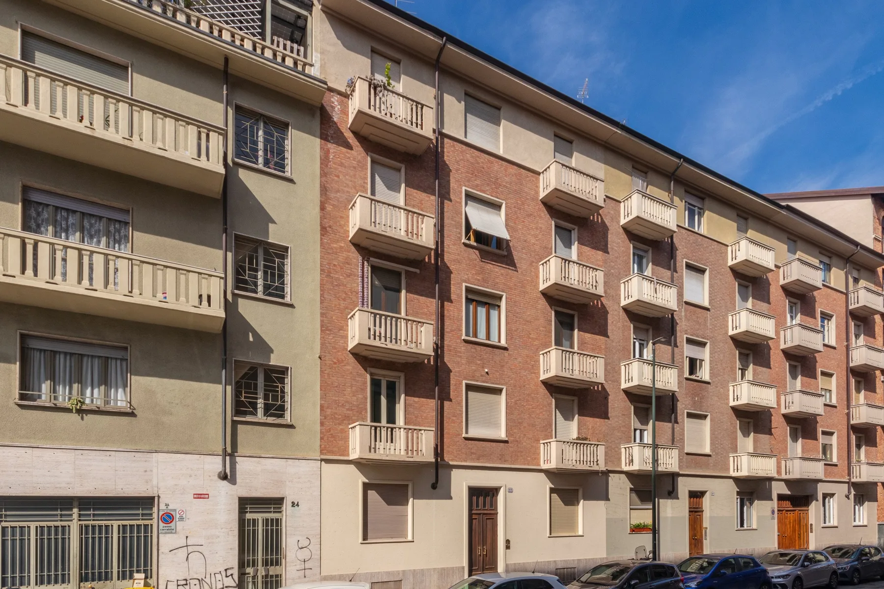 Una fila de edificios de apartamentos de varias plantas con balcones y coches estacionados en la calle.