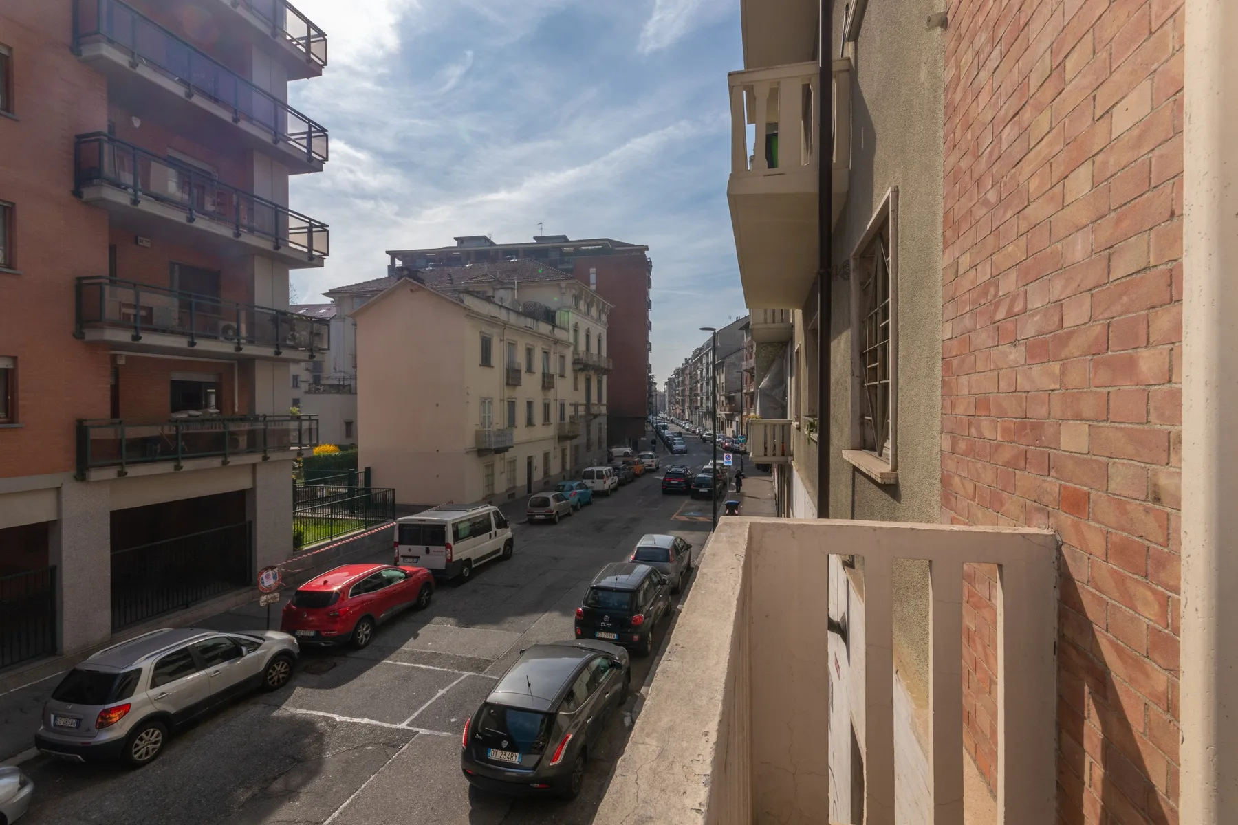 Una calle urbana flanqueada por edificios de apartamentos y coches estacionados.