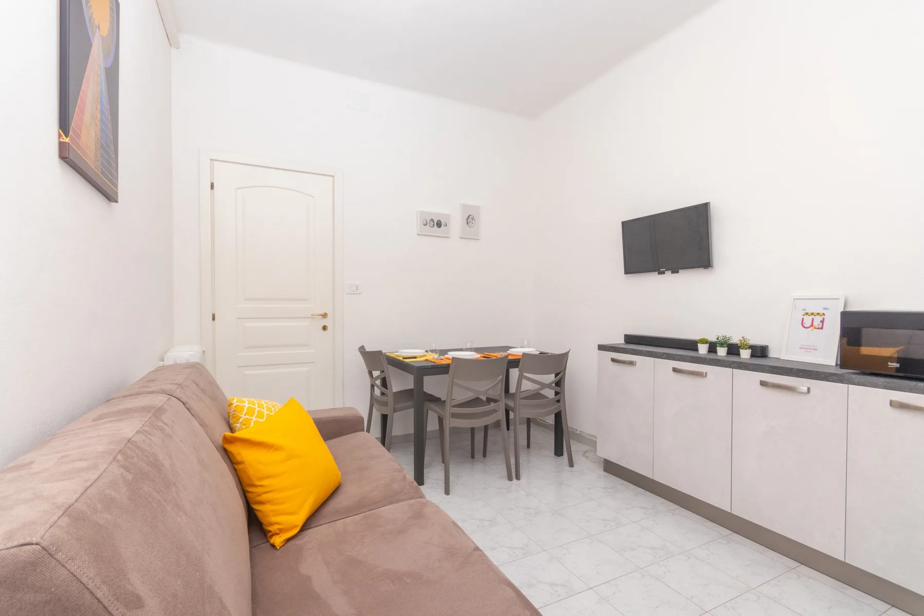 Una luminosa zona de comedor y estar con mesa, asientos y televisor en la pared.