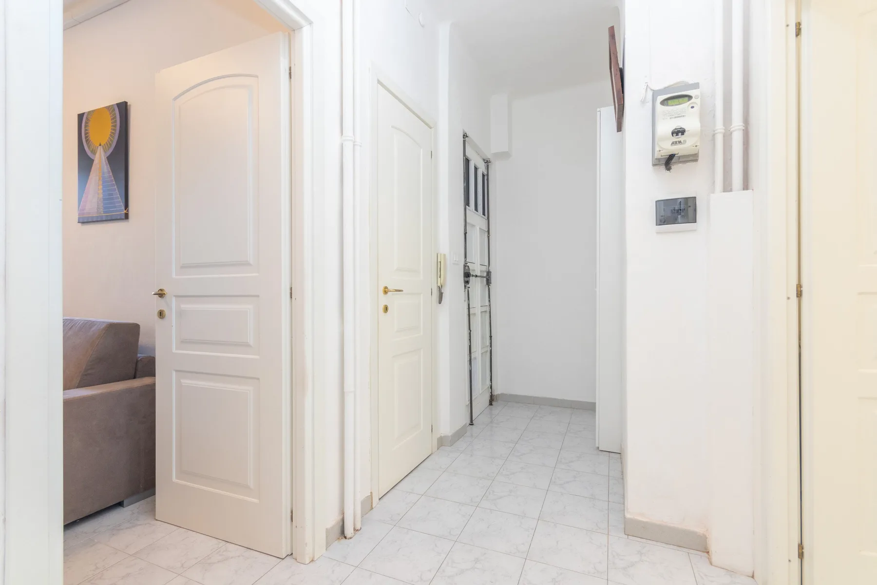 Un pasillo luminoso con puertas blancas, suelo de baldosas y un asiento a la vista.