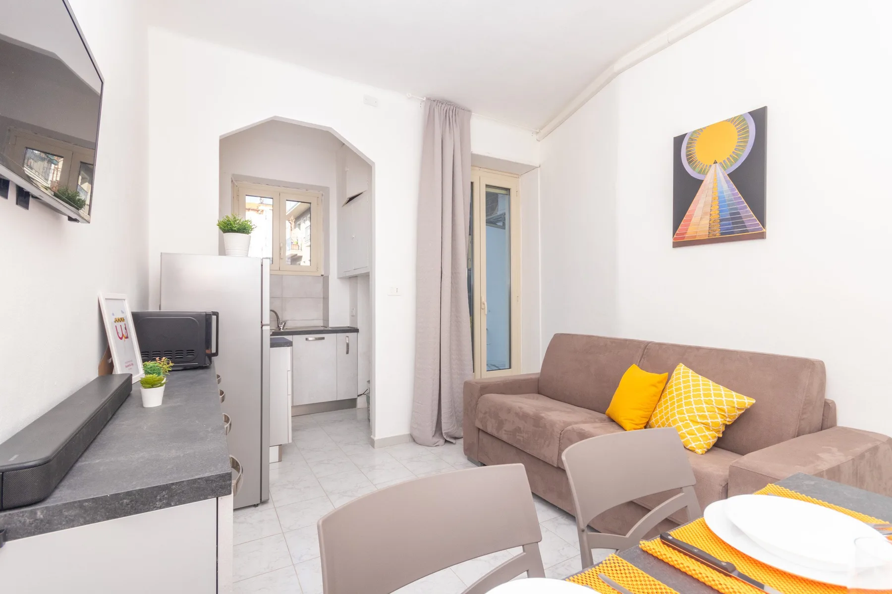 Una sala luminosa con sofá, mesa de comedor y cocina pequeña.