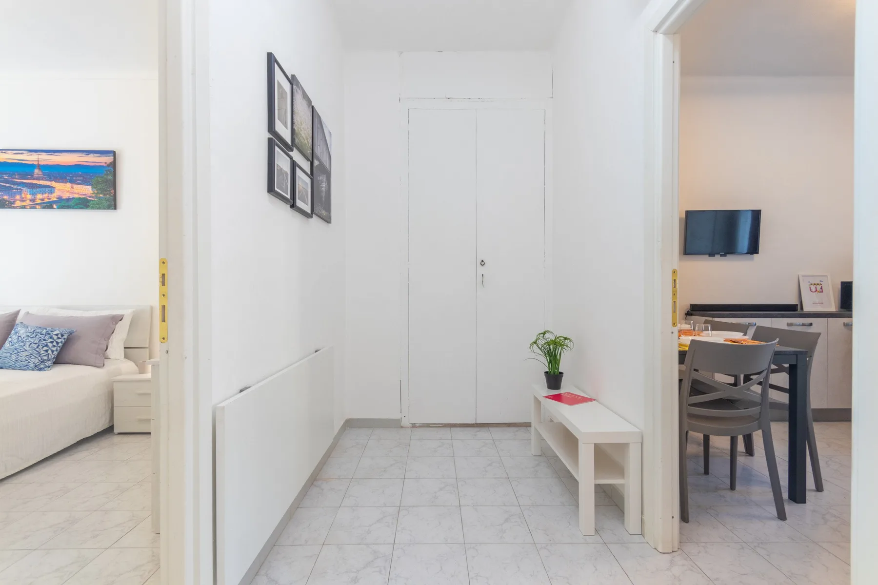 Un pasillo luminoso conecta un dormitorio y un comedor, con un pequeño banco junto a la pared.