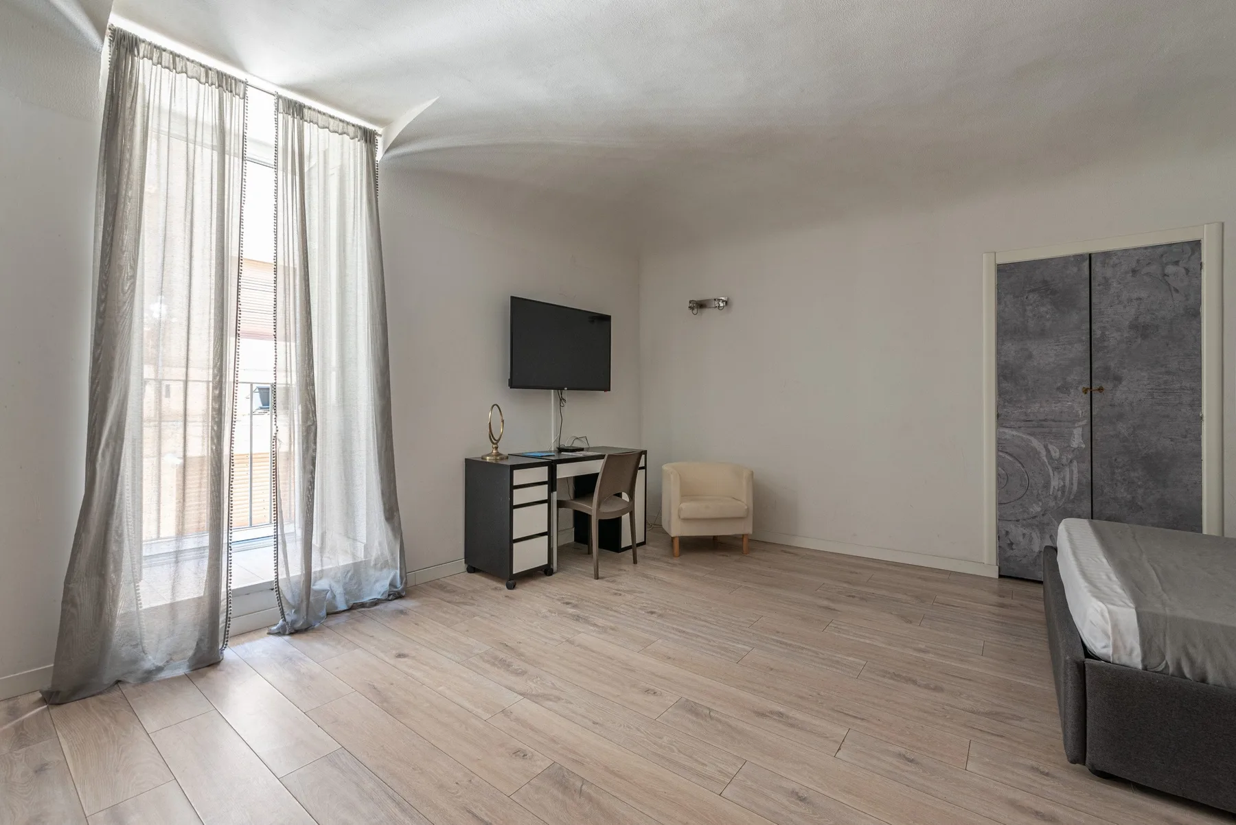 A bedroom with a desk, television, and a bed beside the window.