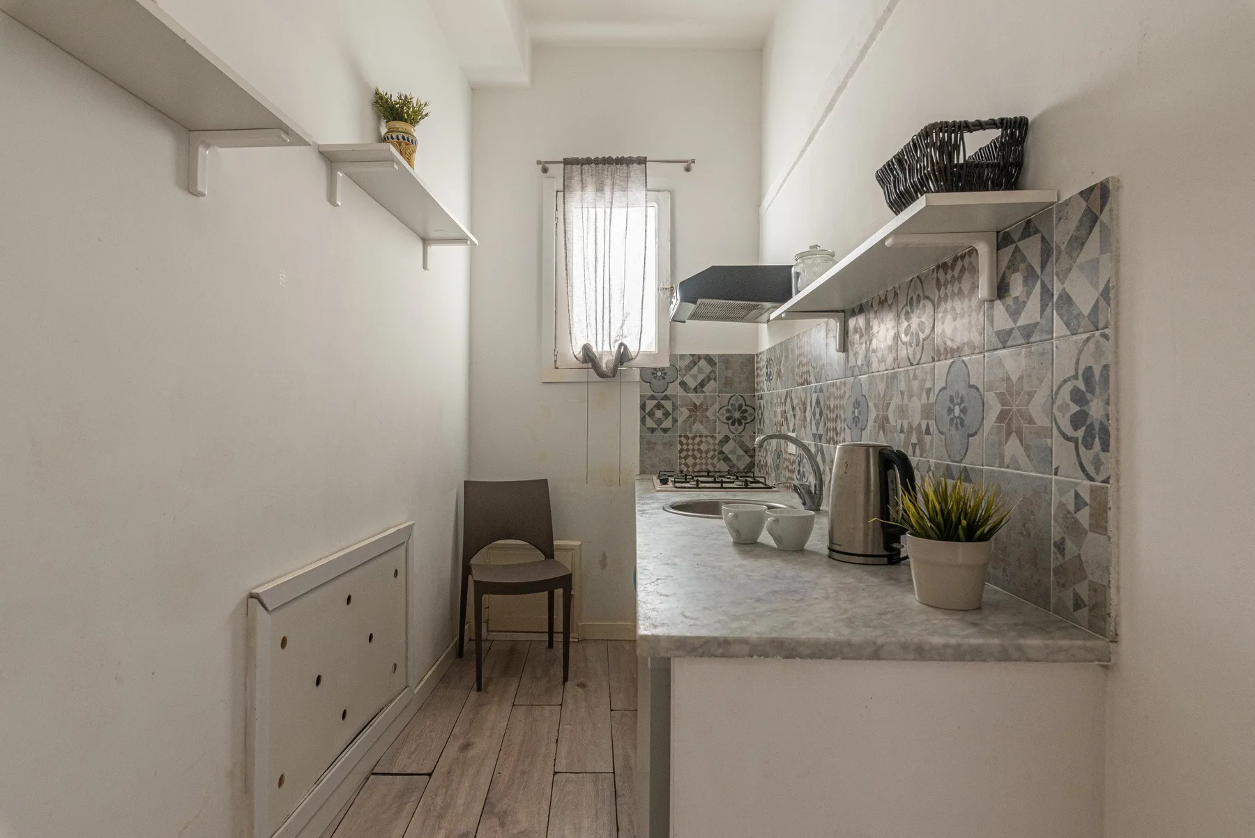 A narrow kitchen with patterned tile backsplash, countertop, and a small table.