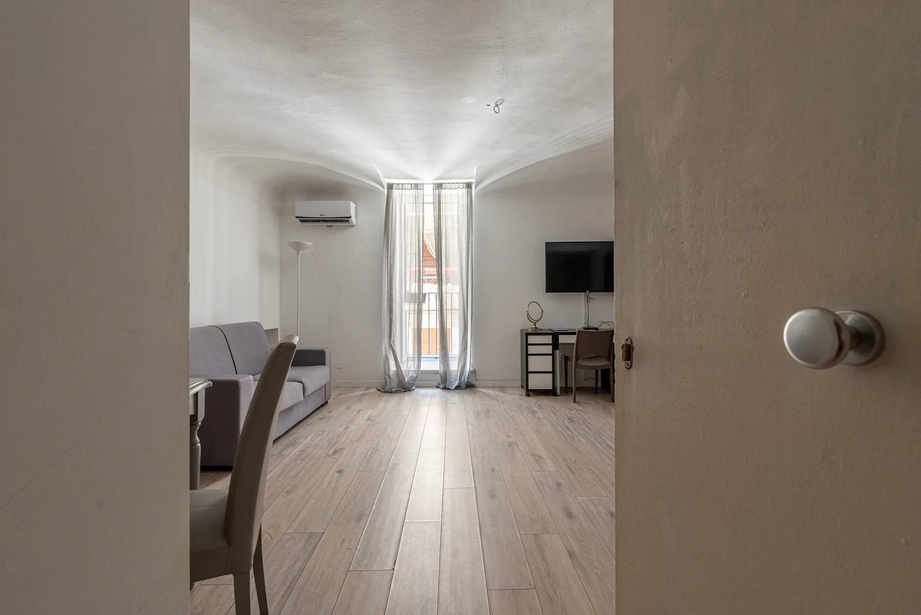 Una sala luminosa con asientos, un televisor y ventanas altas con cortinas.