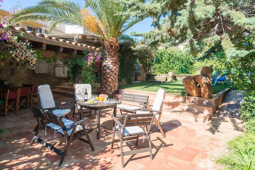 A patio seating area with a table sits beneath palm trees beside a garden.