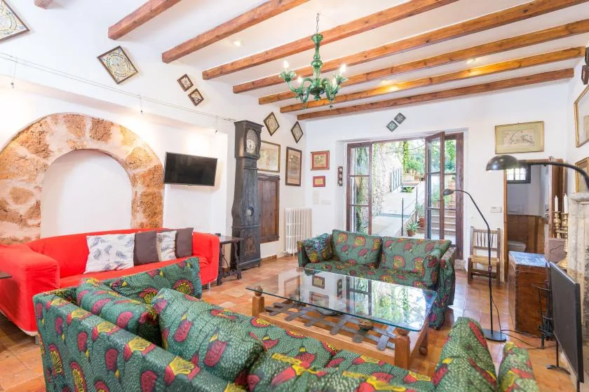 A living room with patterned seating, exposed ceiling beams, and glass doors opening outside.