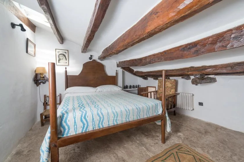 A bedroom with a wooden bed beneath exposed ceiling beams.