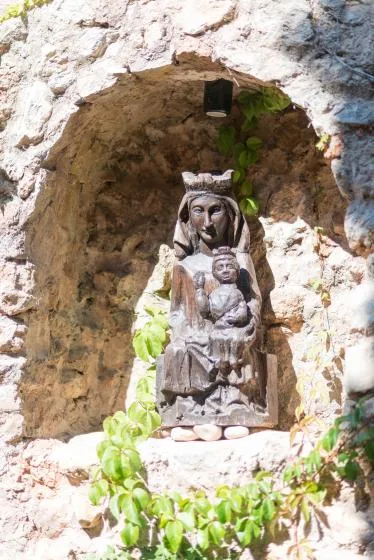 A carved statue of a woman holding a child stands in a rocky alcove.