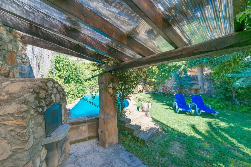 A shaded stone patio overlooks a garden with a swimming pool and lounge seating.