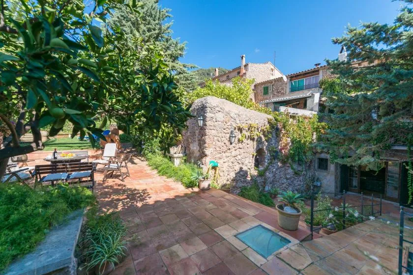 A sunlit stone courtyard with a small rectangular pool and outdoor seating.