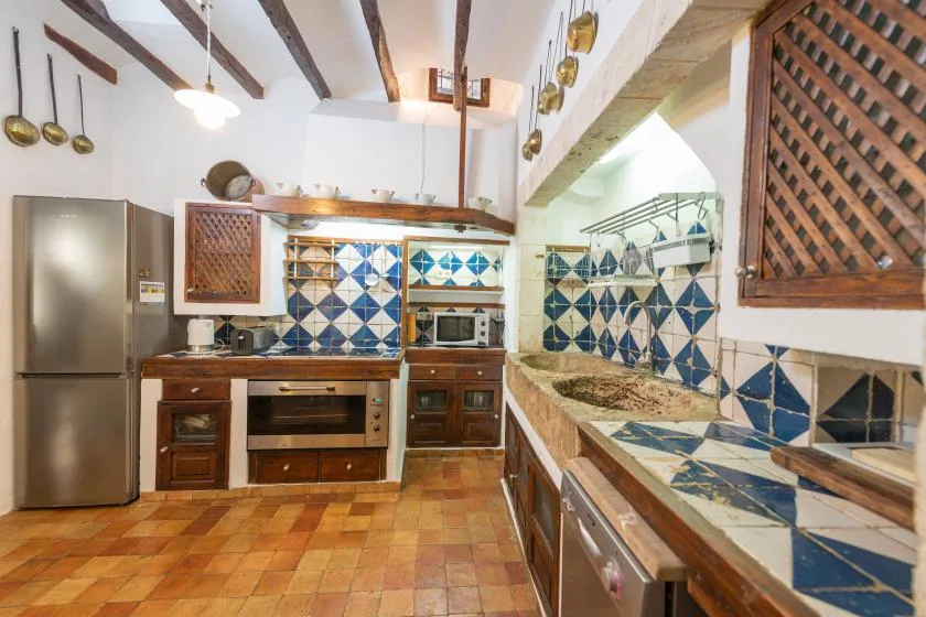 A tiled kitchen with wooden cabinets, a refrigerator, and exposed ceiling beams.