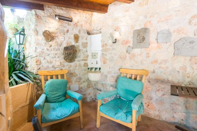 A rustic stone bathroom with two turquoise cushioned seats and a wall-mounted sink.