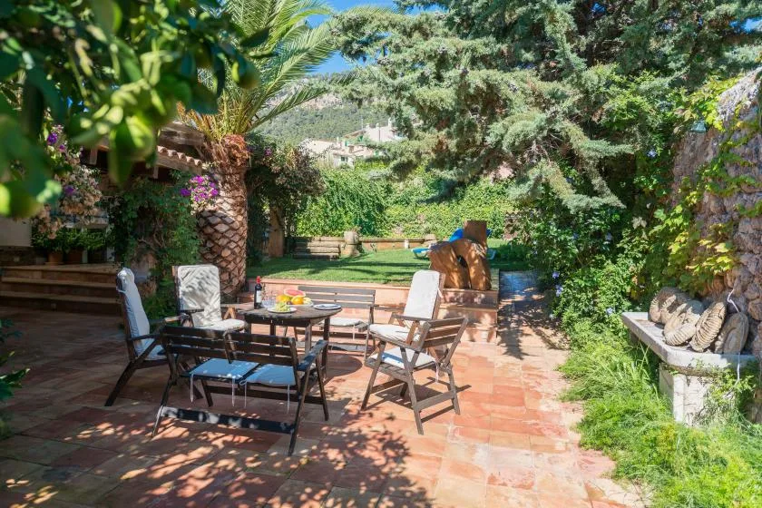 An outdoor patio with a dining table and seating among trees and plants.