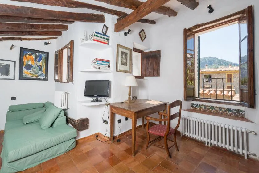 A sitting room with a desk and seating beside an open window overlooking the hills.