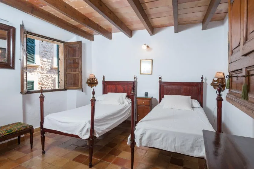 A bedroom with two beds, wooden furnishings, and an open window.