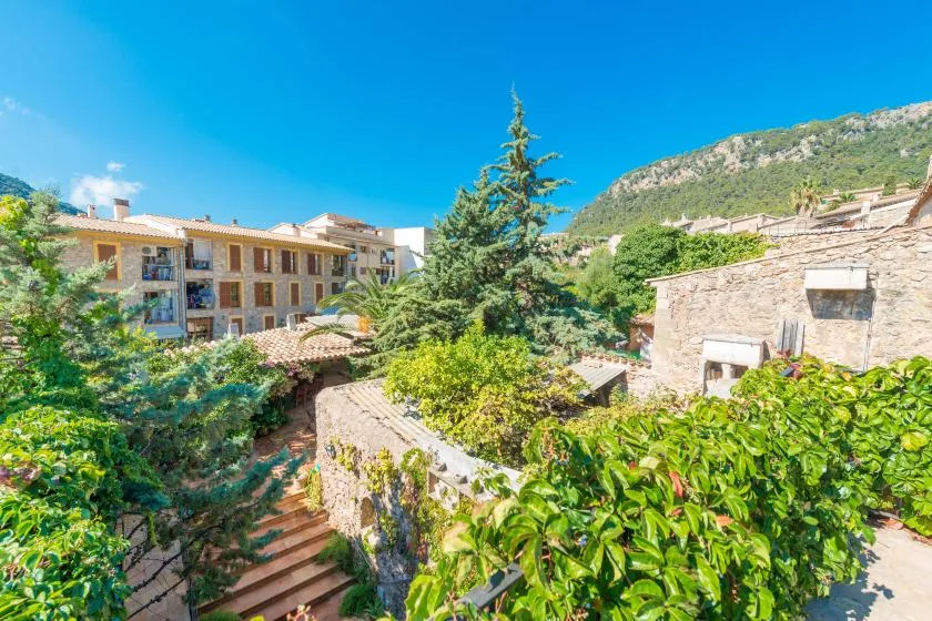A landscaped courtyard with stone buildings, leafy plants, and a mountain slope beyond.