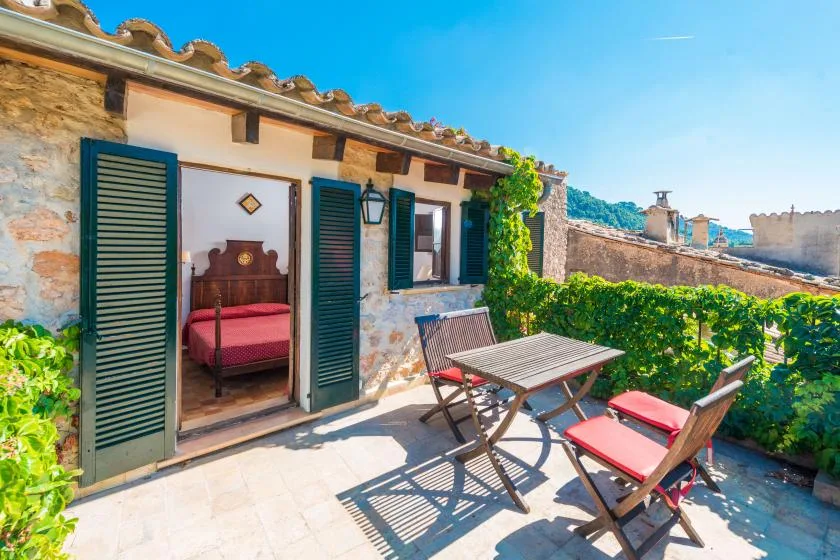 A sunny stone patio with outdoor seating beside a room with open shutters.