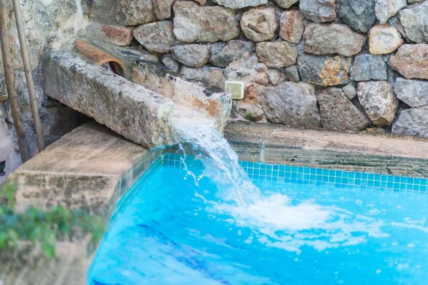 A small pool with water flowing from a stone spout against a rough stone wall.