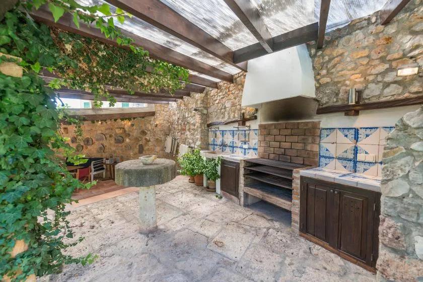 Una cocina exterior de piedra con parrilla y encimera de azulejos bajo un techo cubierto.